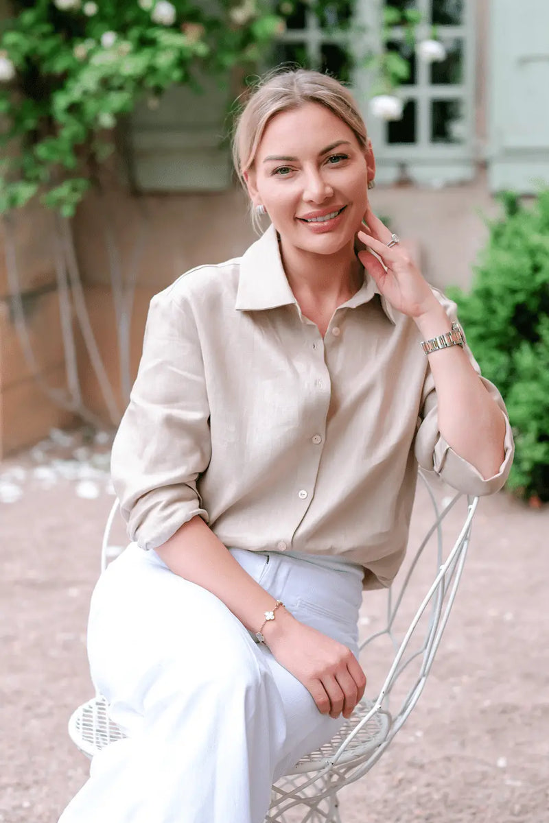 Anna Bey sitting in a garden in a long-sleeved linen shirt in oatmeal