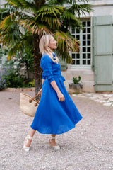 Anna Bey standing in a garden smiling in her signature blue linen dress 